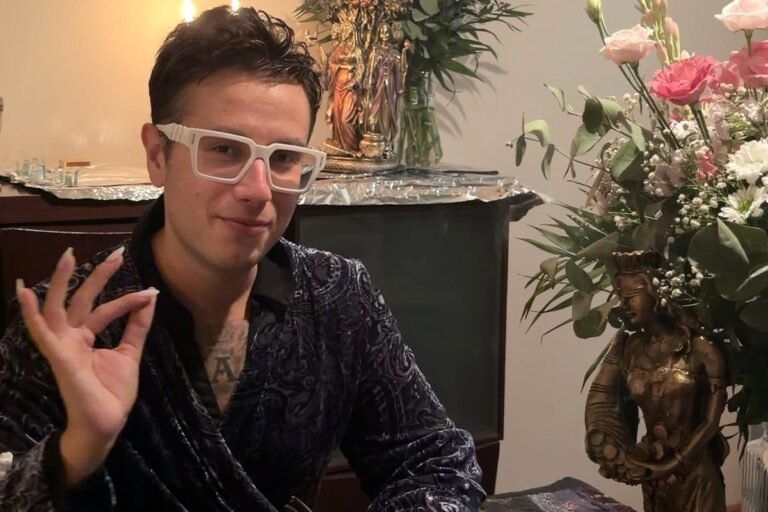 Alejandro, de Tarot de Encarna, con una baraja de cartas en la mano ante una mesa con flores y figuras ceremoniales